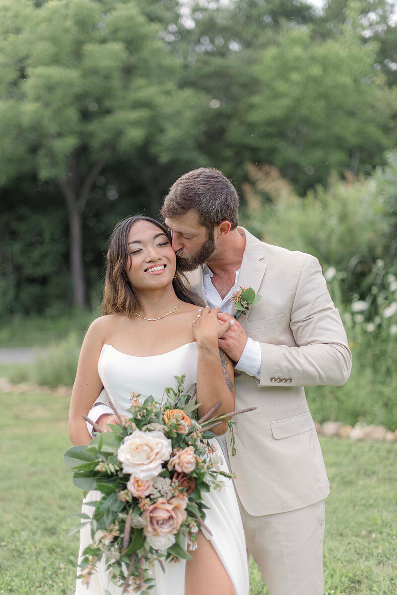 New couple pose lovingly as groom kisses his bride's cheek