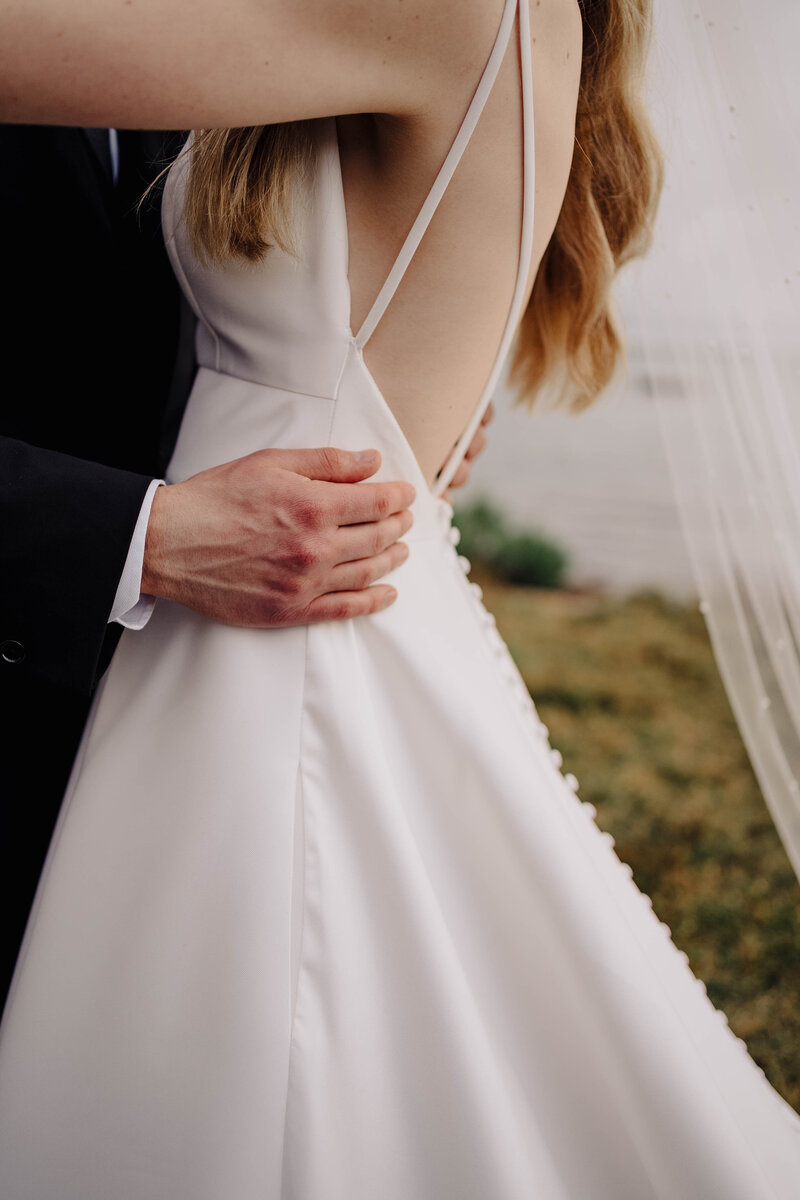 Close-up shot of groom's hands embracing bride wearing low-back satin wedding dress with buttons down the back. Photo taken by Orlando Wedding Photographer Four Loves Photo and Film.