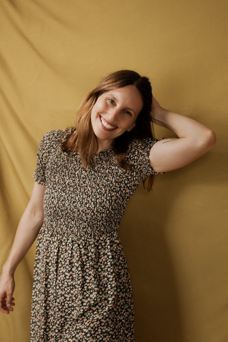 A person smiling with one hand on the back of their head 