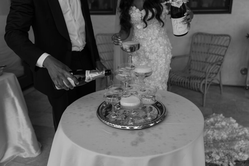 Bride and groom pouring champagne in their champagne tower after their wedding ceremony, in black and white..