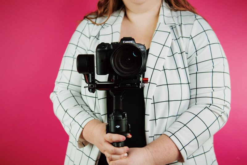 mara shields in front of a pink backdrop. photo is cropped from the chin to waist, showing a white blazer with black checker stripes, and my camera and gimbal