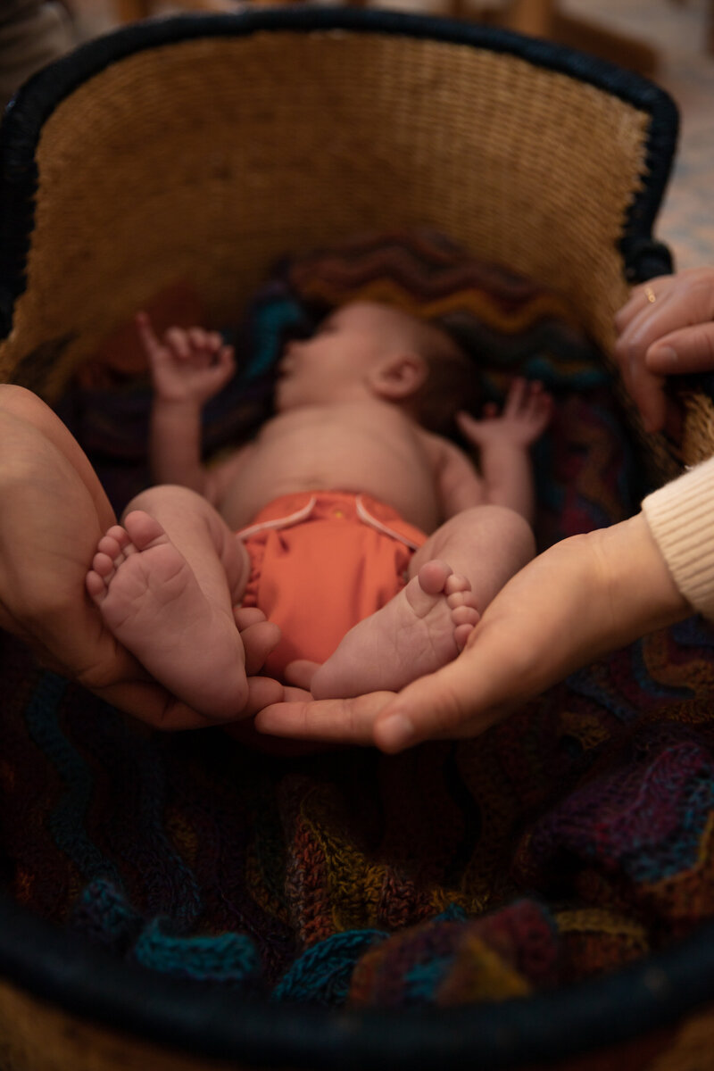 mother and father hold newborn baby's feet in hands while baby lays in moses basket