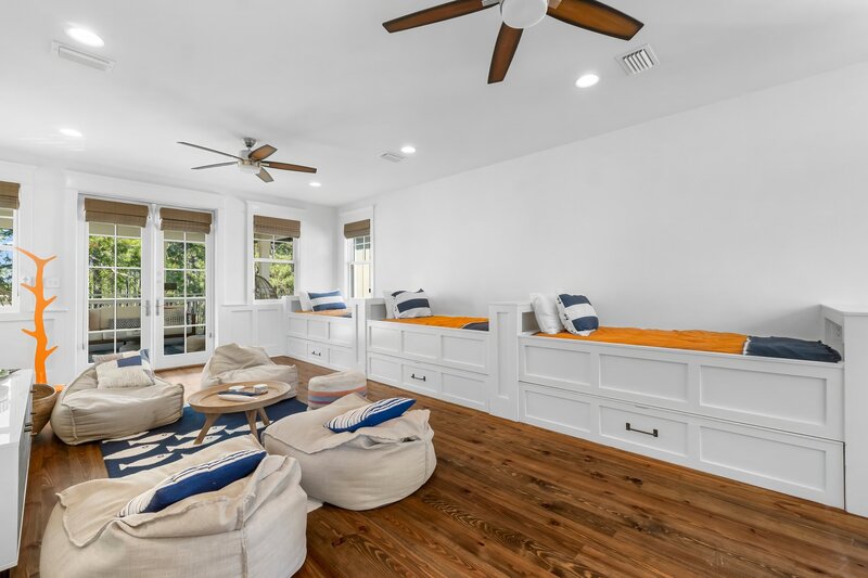 Spacious upstairs hangout with three built-in twin bunks, beanbag chairs, ceiling fans, and balcony access at family-friendly 30A vacation home.