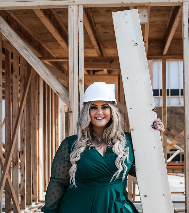 Stefanie Couch is on aa construction jobsite with a hardhat and a piece of lumber.