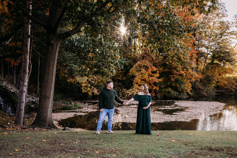 Expectant couple holds hands amongst a beautiful fall sunset