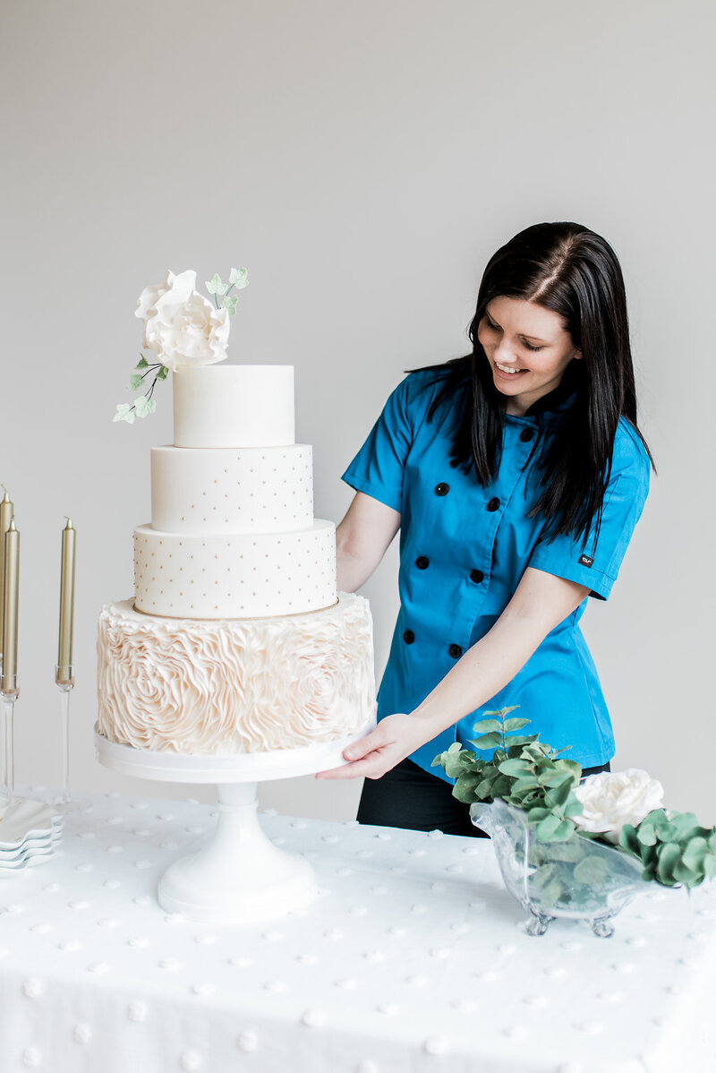 Cake artist looking at wedding cake with blush ruffle rosettes and sugar flowers.