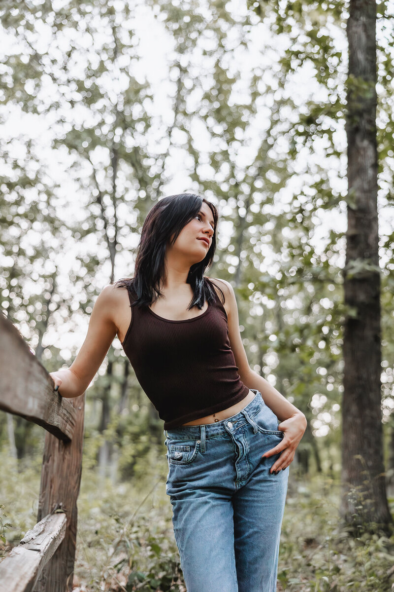 Senior girl leaning on wooden fence in the woods. 