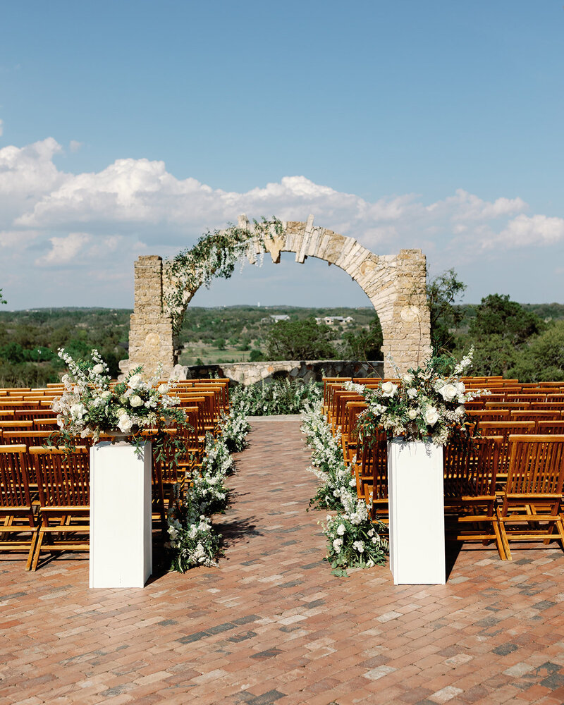 Outdoor wedding ceremony setup with romantic white floral arrangements and hill country views, styled in Central Texas.