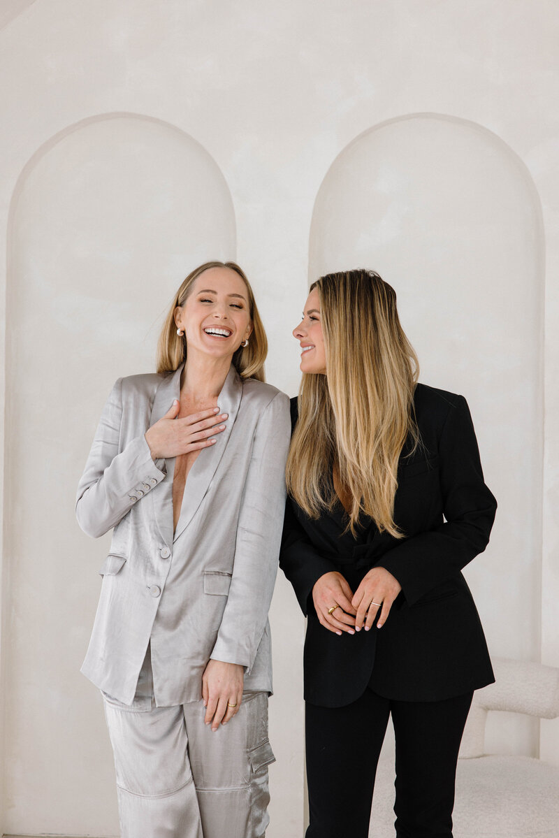 Two females, one in a silver suit, one in a black suit laughing together