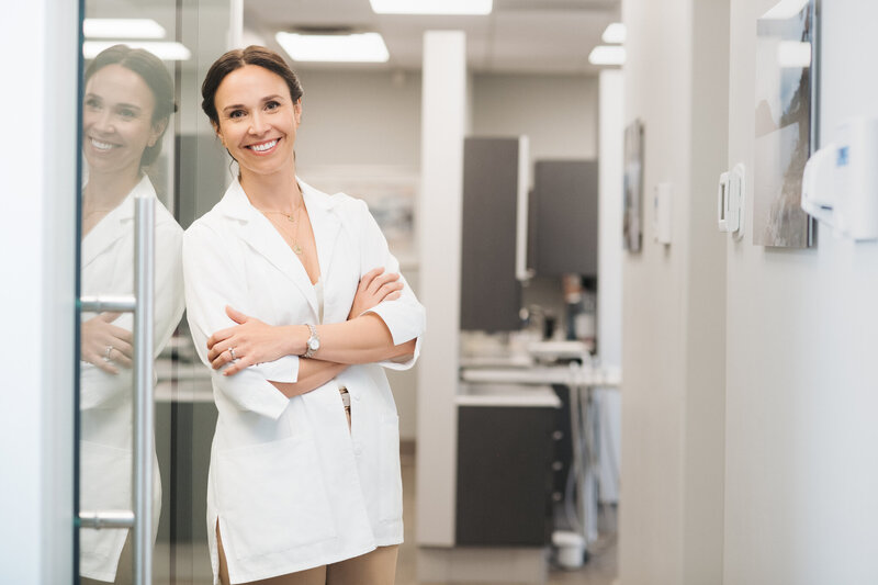 Dr Heather Dagenais leaning on a glass door with her arms crossed and smiling