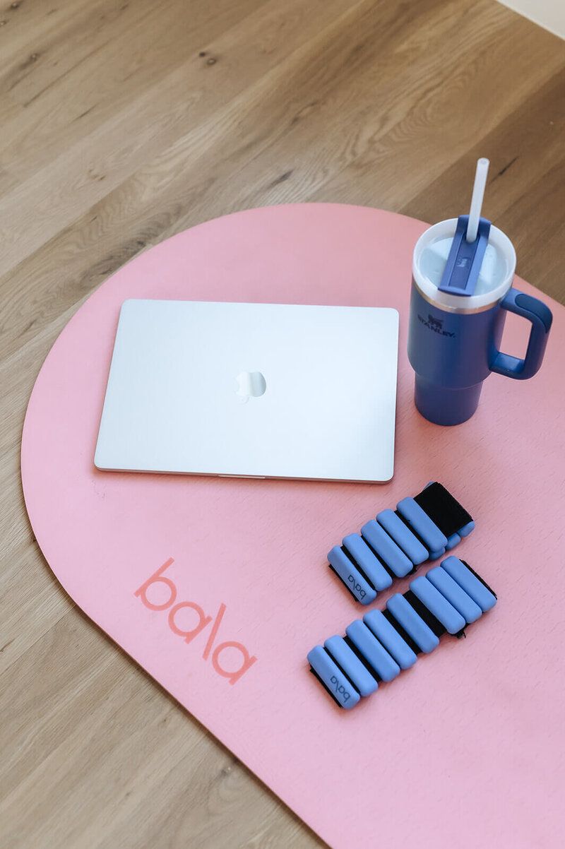 Flatlay of laptop, water cup, and Bala weights on pink mat—representing Erica Taylor Wellness quiz for moms to explore their real-life wellness style