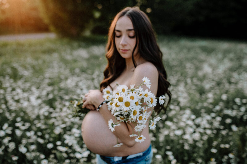 Pregnant Person standing holding daisies