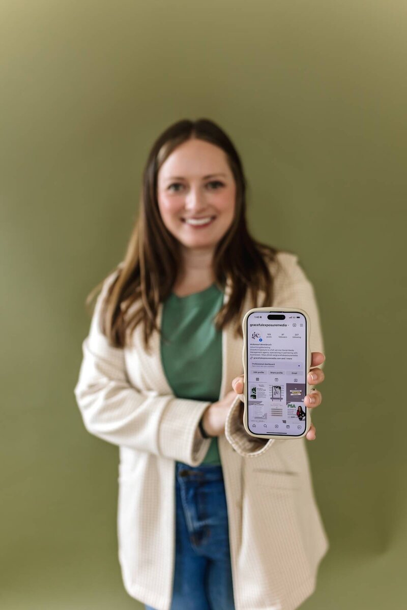 McKenna Fahrenbruch from Graceful Exposure Media holding up her phone with a curated Instagram feed displayed, showcasing expert social media management and content strategy services.