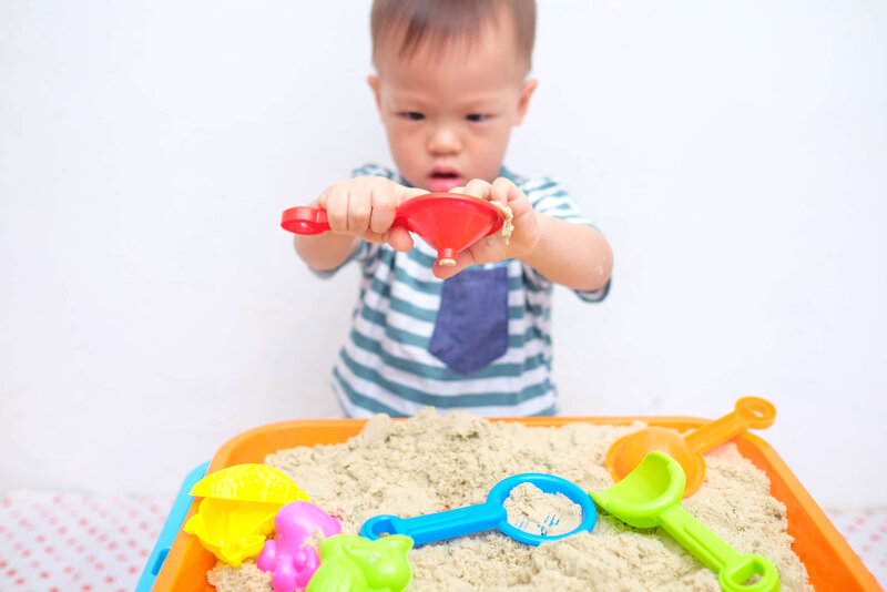 toddler playing with colorful toys in the sand