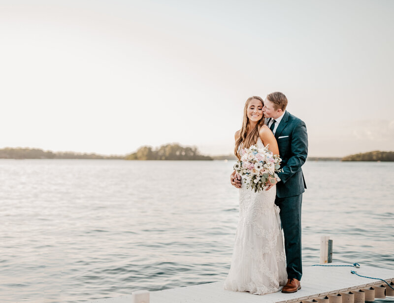 a bride standing behind her groom hugging him under a tree