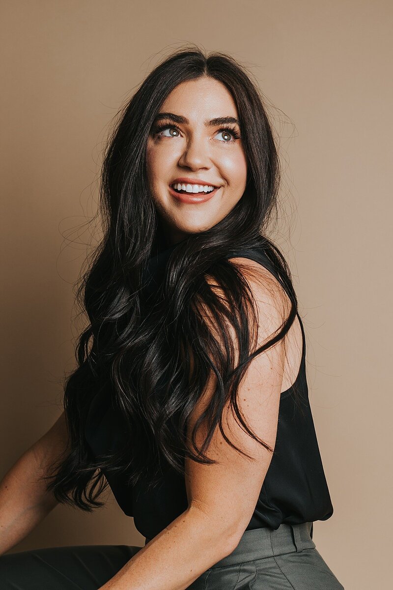Colorado wedding photographer sitting in a studio with a tan paper backdrop, smiling for a headshot