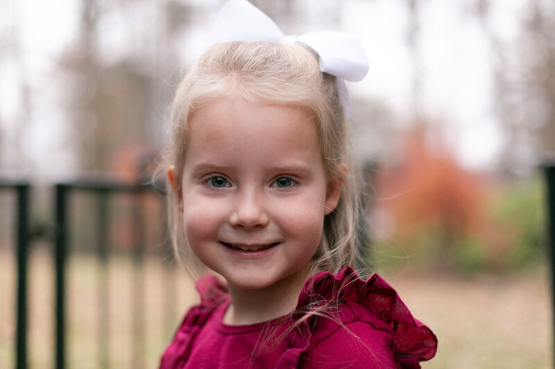 4 year old girl with burgundy shirt and white bow smiling at camera