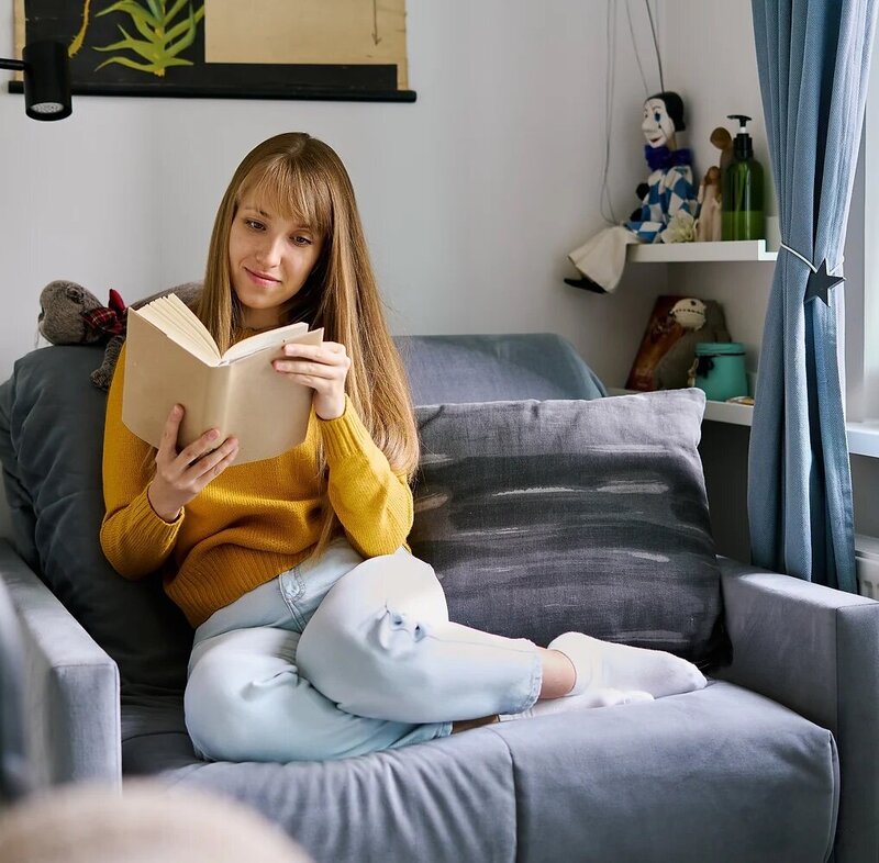 Woman sitting on couch and reading book_ Social media detox_ Slow living lifestyle_ Mental
