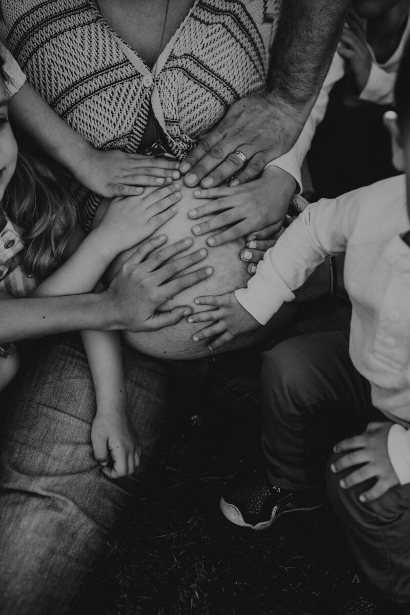 A family with 6 kids placing their hands on their mothers pregnant belly during maternity photos