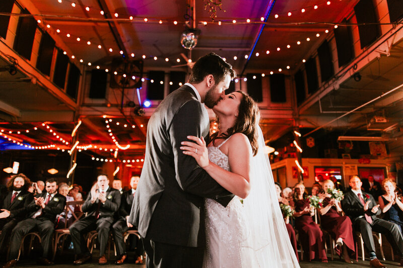 Wedding couples first kiss photographed towards the guests. Wedding was at the Maumee Bay Brewing Co in Toledo Ohio
