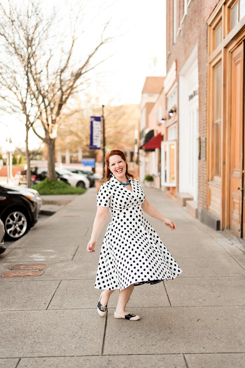 Event planner in downtown Murfreesboro Tennessee wearing a black and white polka dot dress while spinning and smiling at the camera