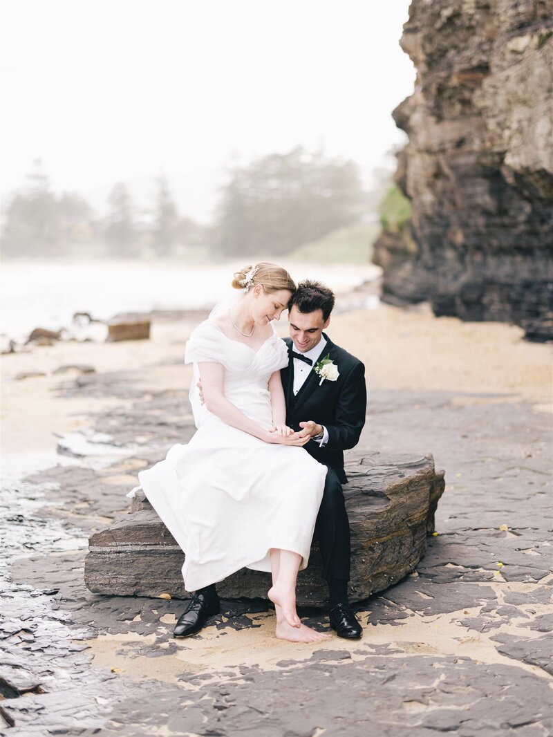 Bride and groom sitting at beach looking at wedding rings