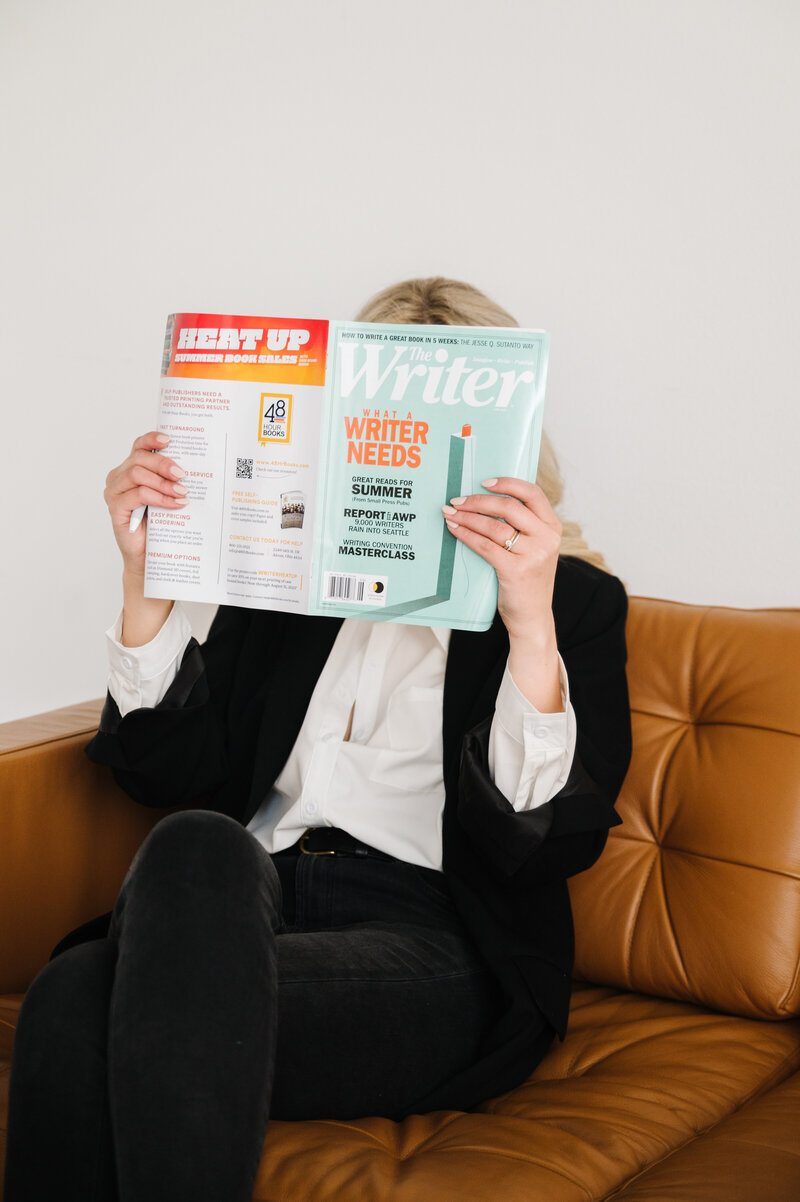 Sarah Klongerbo sitting on a leather couch holding an open magazine in front of her face