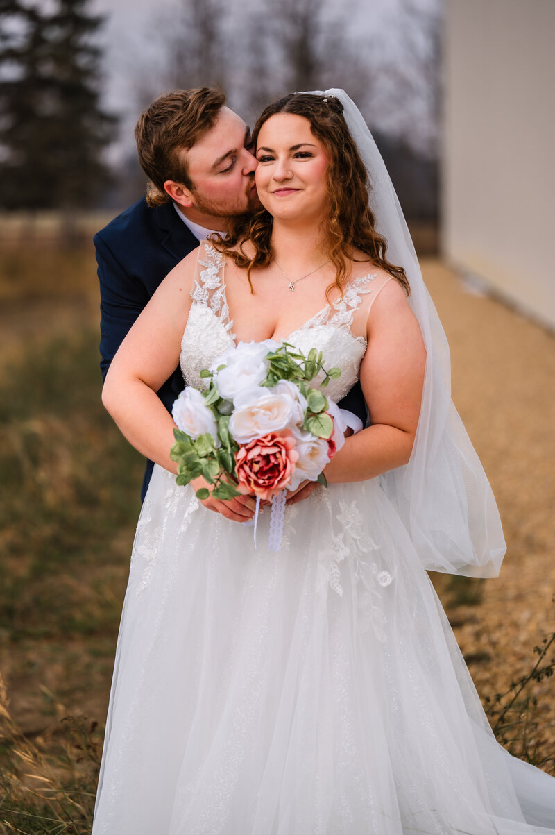 groom gives bride a kiss on the cheek at their country wedding near Westlock, Alberta