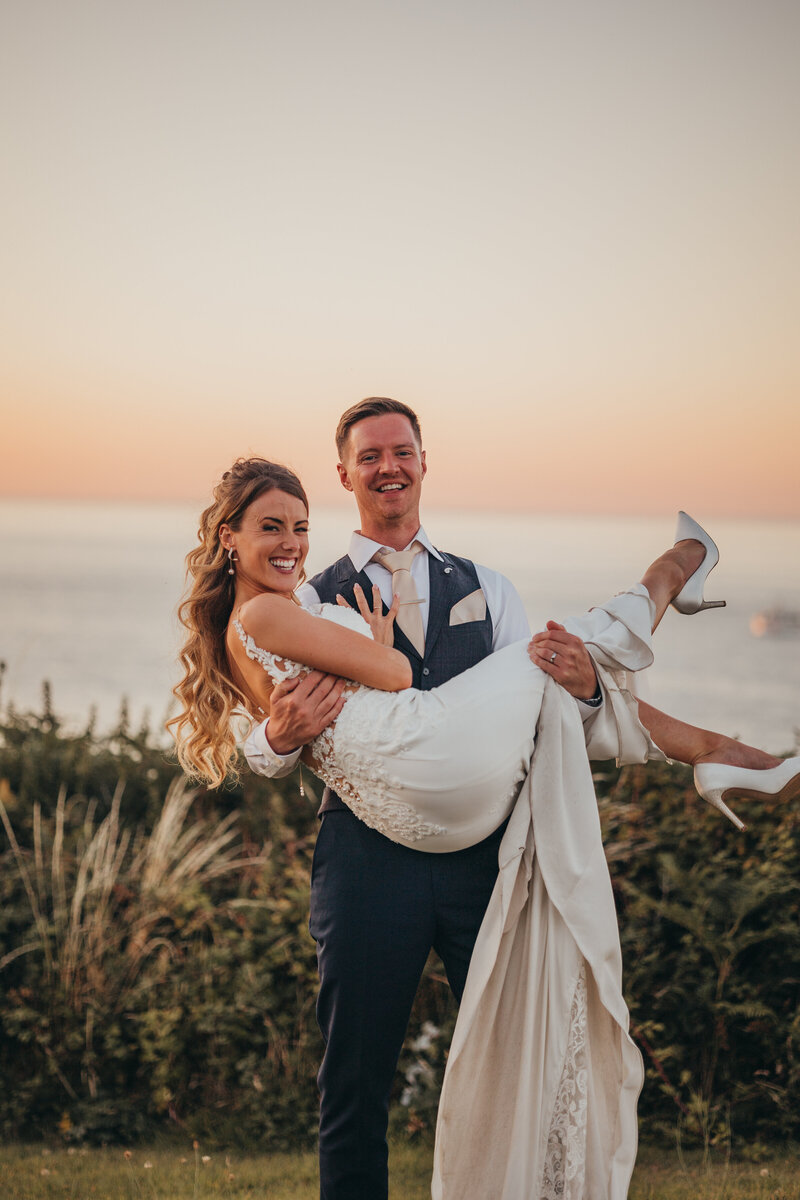 groom holds his bride by the ocean