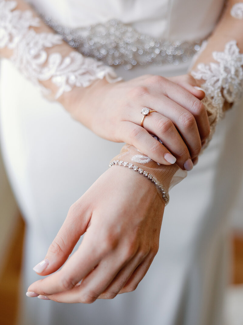 A closeup of a bride's hands showing her engagement ring, diamond bracelet, and beaded dress details.