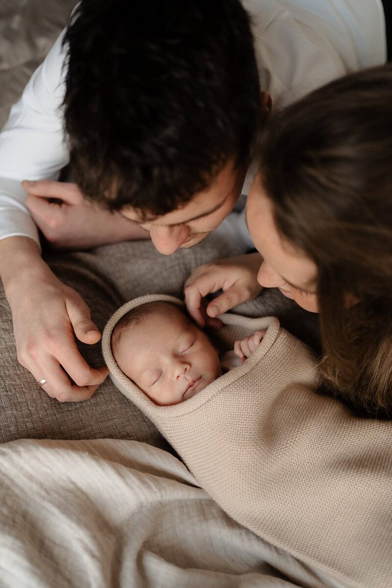 Gezin kijkt naar slapende pasgeboren baby tijdens newbornshoot, gefotografeerd door familiefotograaf Julia de Groot