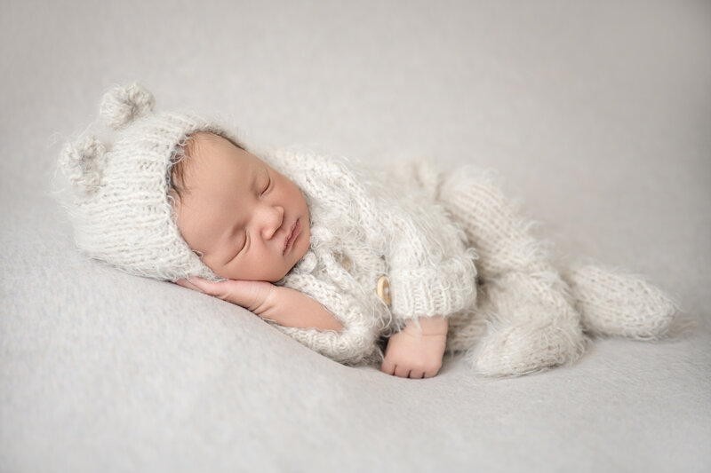 newborn baby boy sleeping in a cream fuzzy outfit