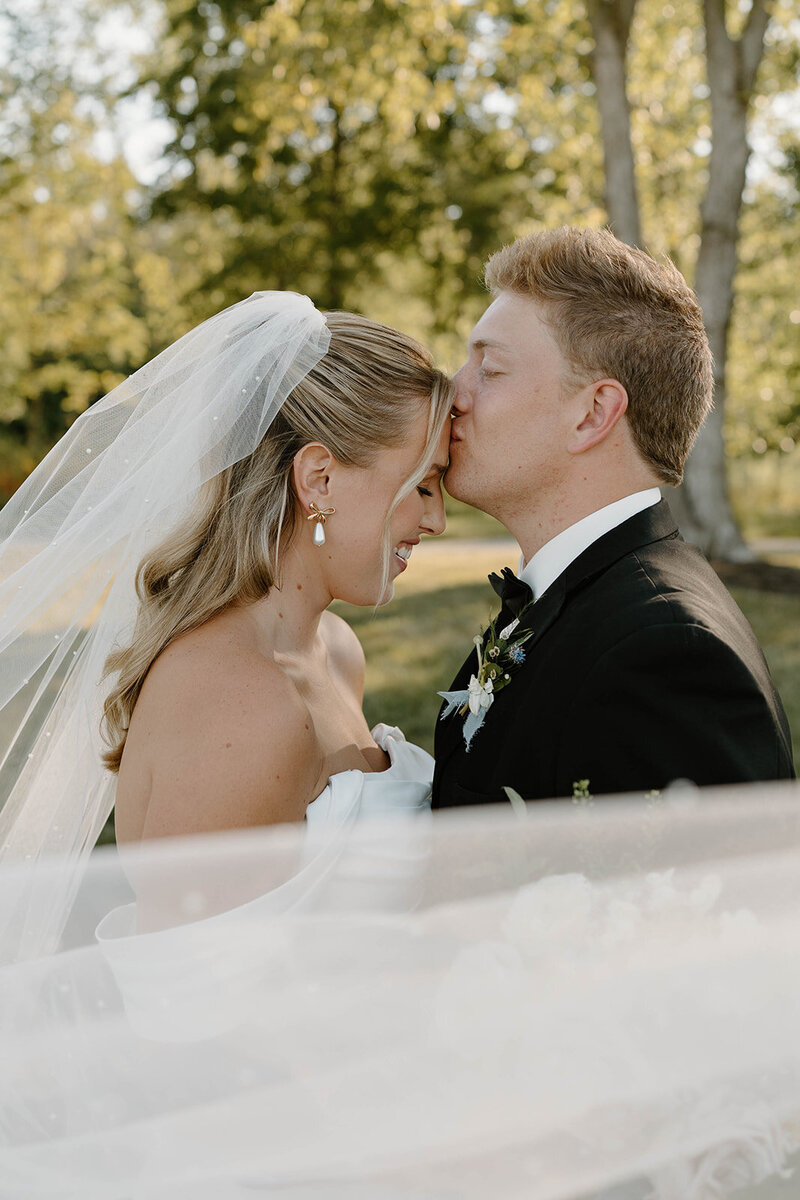 Romantic moment captured under the bride's veil as the groom gently kisses her forehead, a tender expression of love and affection on their wedding day in Columbus, OH.