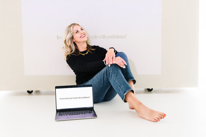Sarah Klongerbo sitting against a white wall on a floor covered with newspaper pages