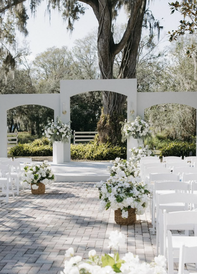 Outdoor wedding ceremony setup at Uliana Estate in Lakeland, Florida, featuring white arches, elegant white florals, and rows of white chairs beneath oak trees