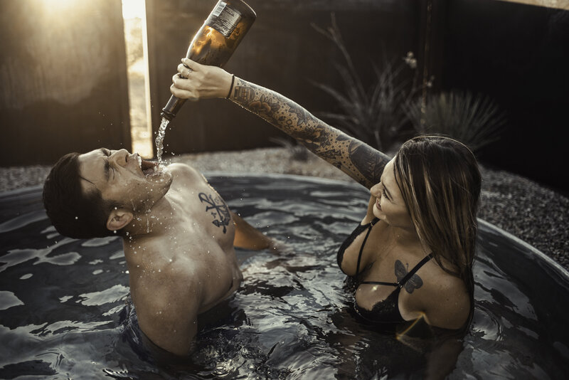 wife pouring champagne in husbands mouth during intimate steamy session in the outdoor bath in an AIRBNB in Joshua tree