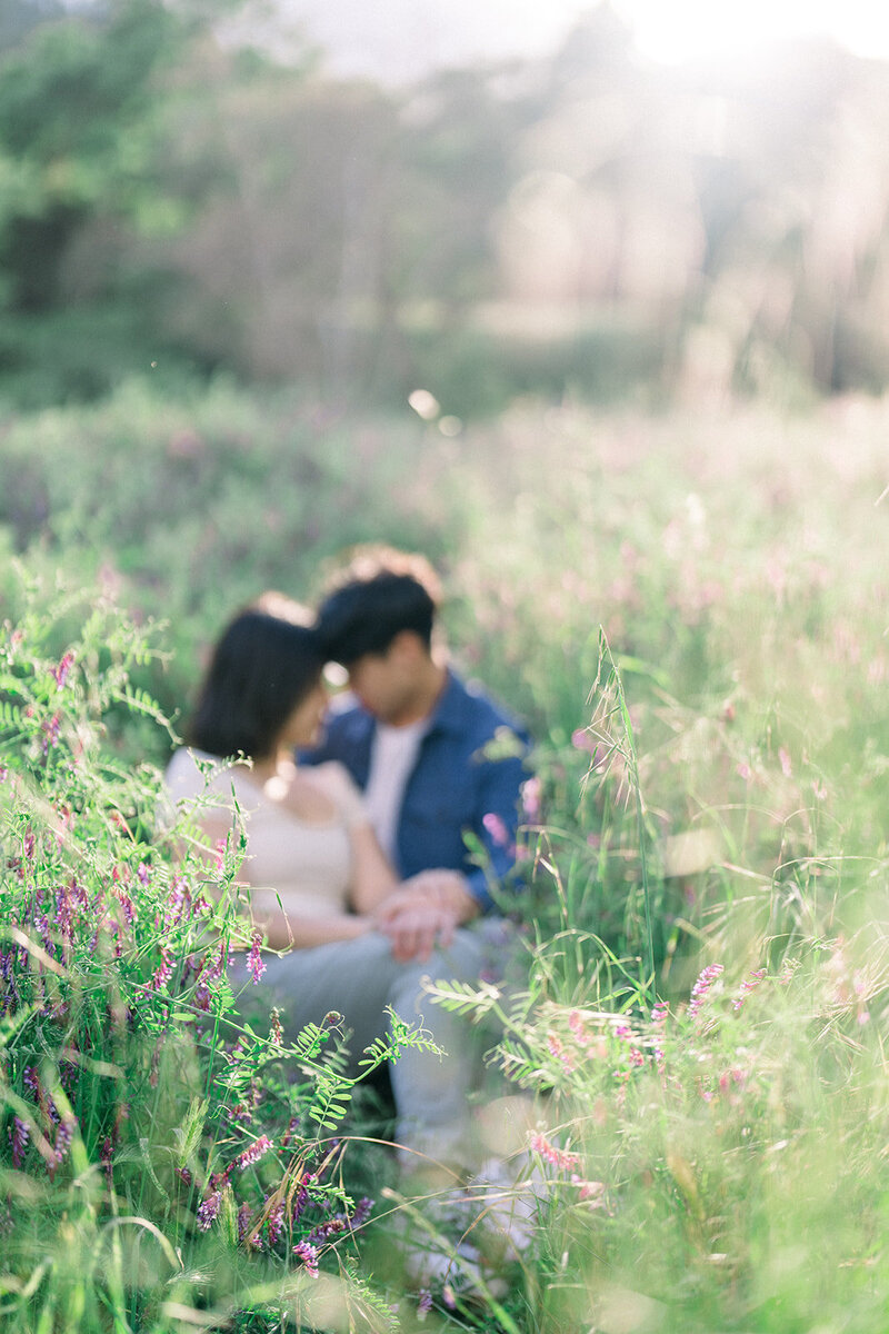 A couple sits in a whimsical meadow surrounded by wildflowers during their engagement session at Descanso Gardens in Los Angeles, California, captured by Tiffany Longeway Photography.