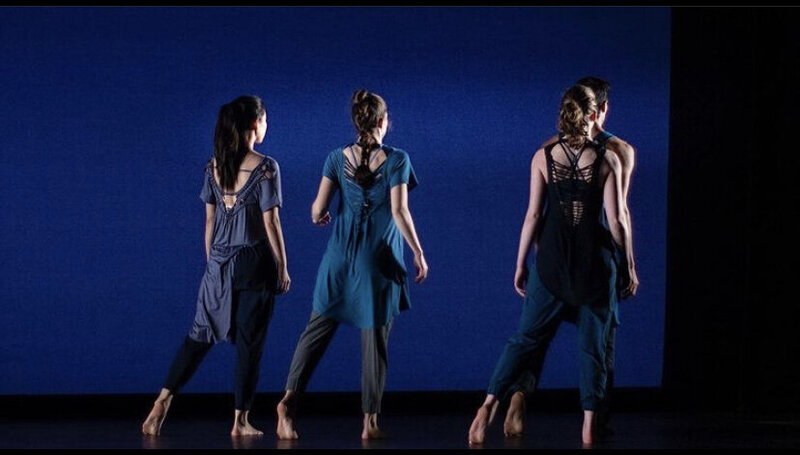 Three woman on a stage with a dark blue background, they are slowly walking away from the audience