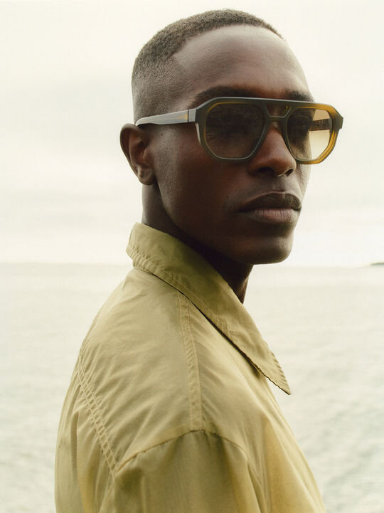 Close shot of man with MYKITA sunglasses and yellow-green collared shirt in front of a white background