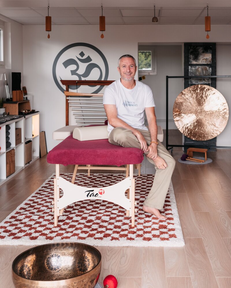 Lydéric Auclair, sonothérapeute, est assis sur une table de massage sonore entouré de ses instruments