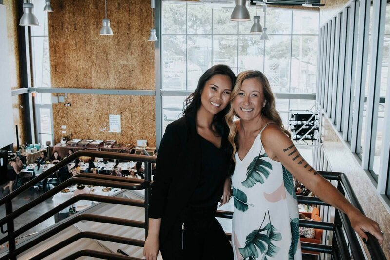 founder michelle is wearing an all black outfit standing next to a smiling woman in a white dress with palm pattern at hawaii event