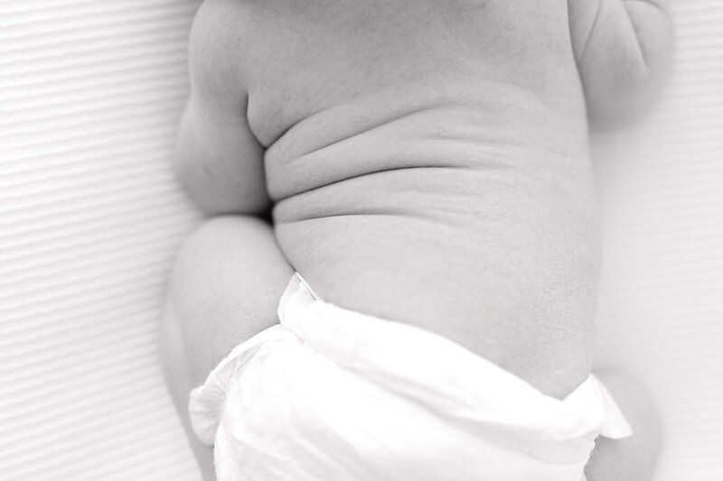 A black and white image of a baby's back with the focus on the rolls  of their tummy.
