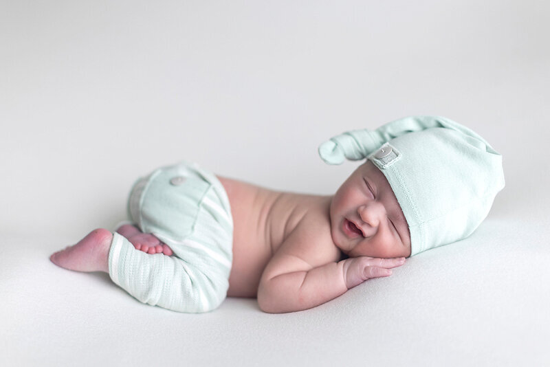 Newborn boy smiling on white fabric.