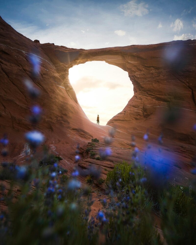 Image of a person hiking in a rock formation with an arch above them.