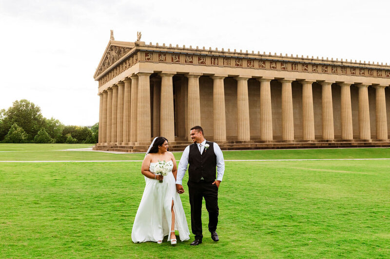 Newlyweds walking together in wedding attire outside of Parthenon in Nashville
