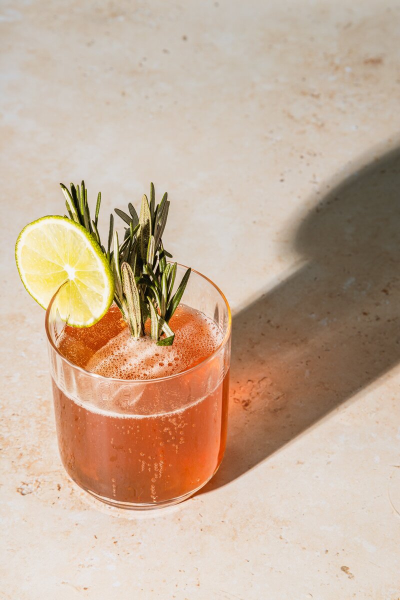 a  glass filled with a drink and no ice with a rosemary garnish and lime circle for the contact page socialfizz