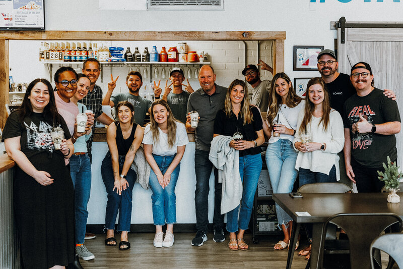A diverse group of people stand for a group photo smiling at an ice cream shop.