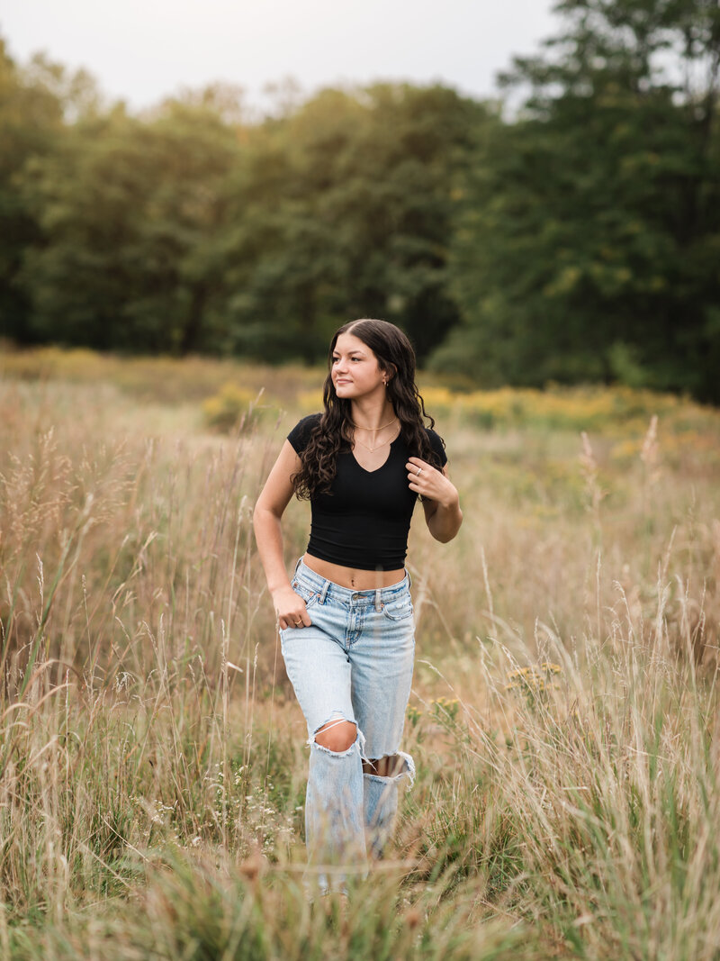 senior girl in black shirt and jeans walking through field for senior photos Cleveland family photographer