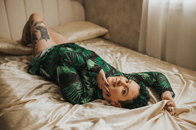 queer person poses on bed in dress during boudoir photography session