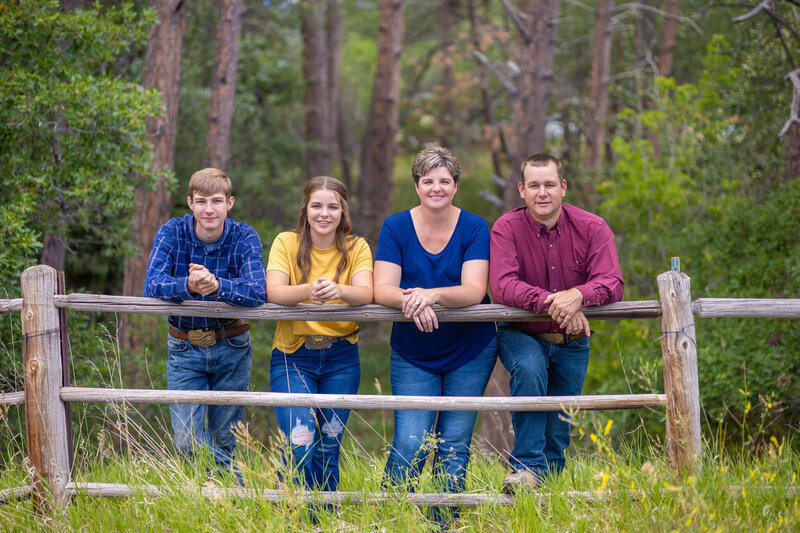 family of four standing next to each other leaning against a wooden fence
